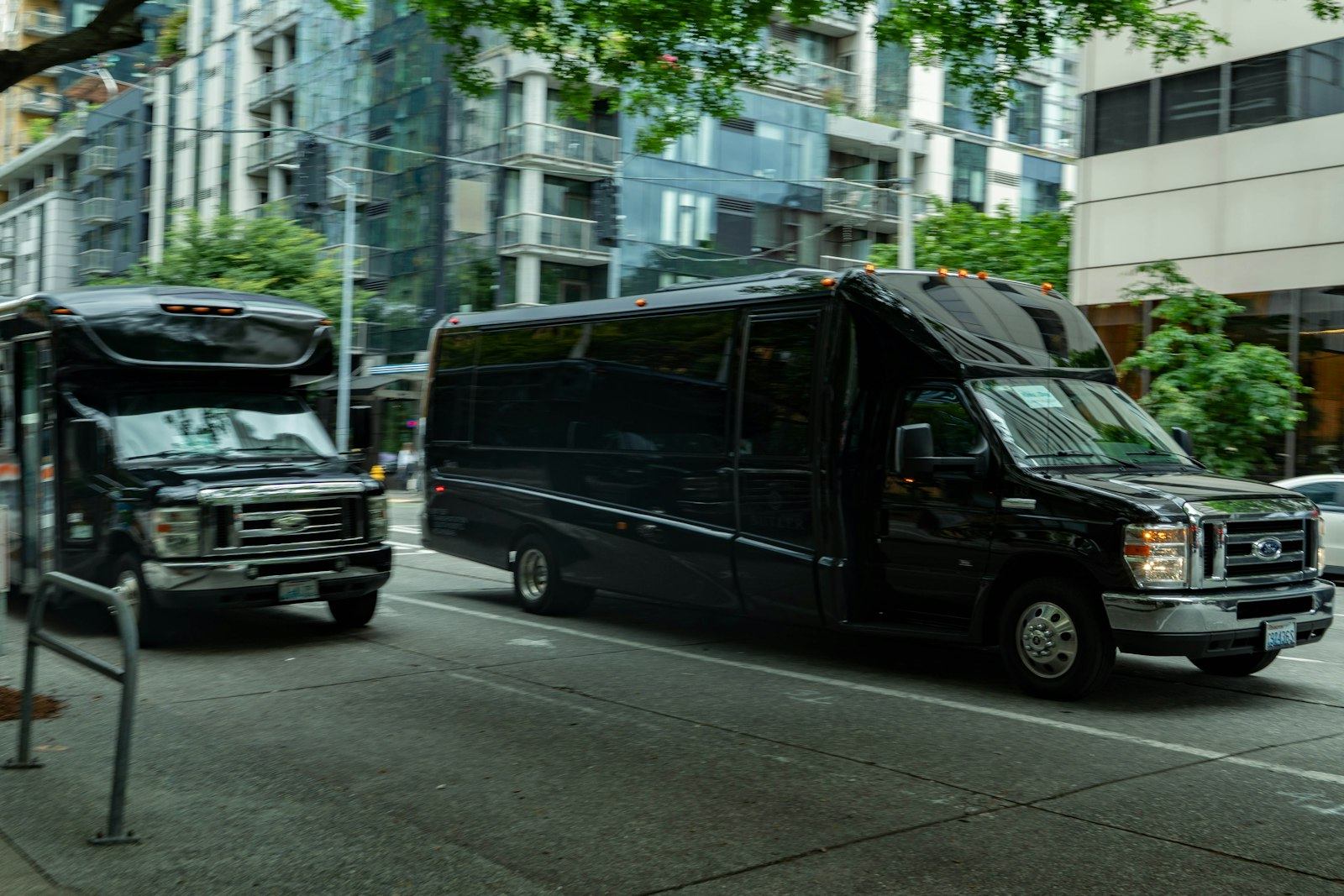 Two black charter buses picking up a group on a downtown street