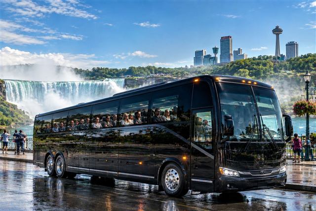Black bus from our fleet parked in front of Niagara Falls and the Skylon Tower